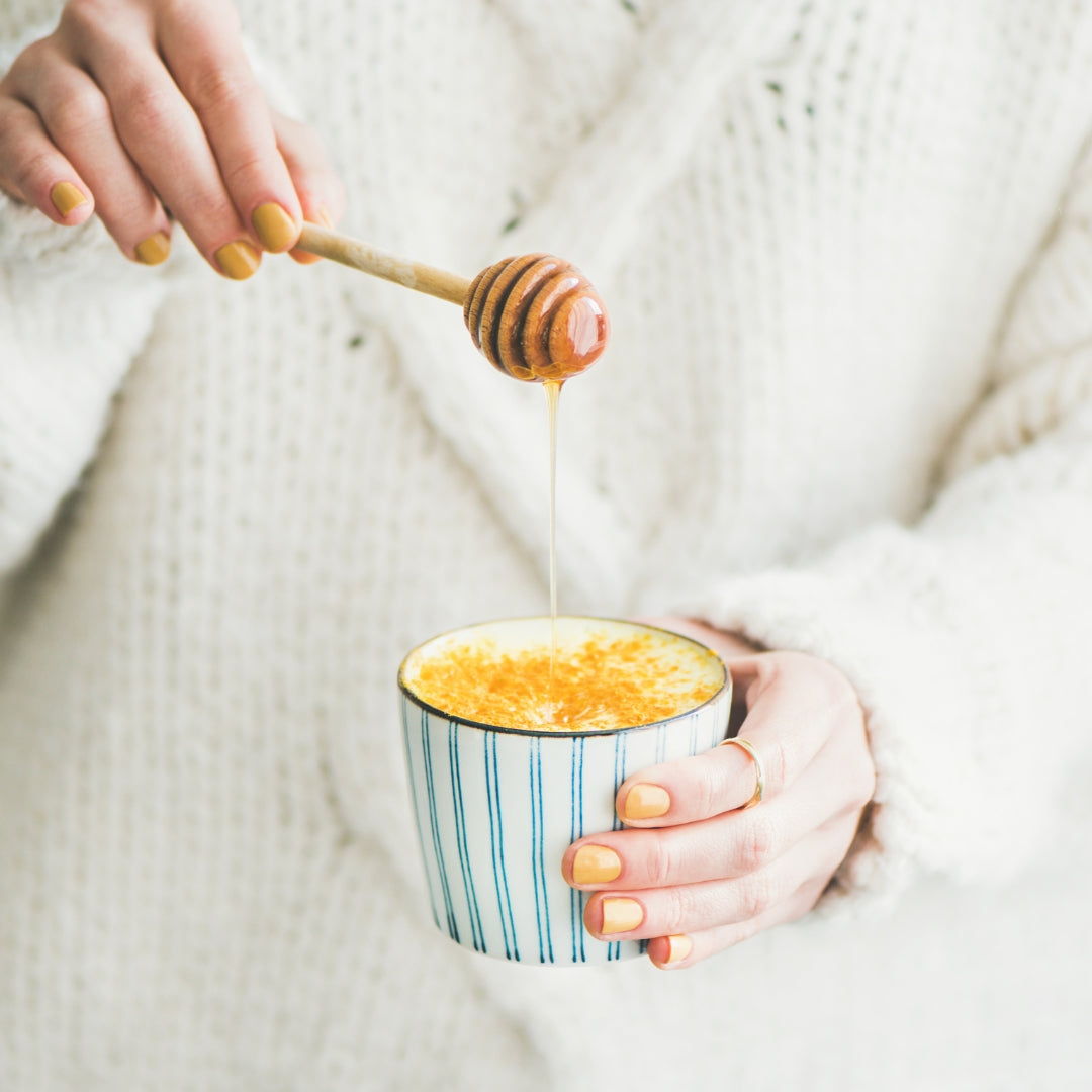 lait doré dans un tasse, femme avec un pull blanc, bâton de miel