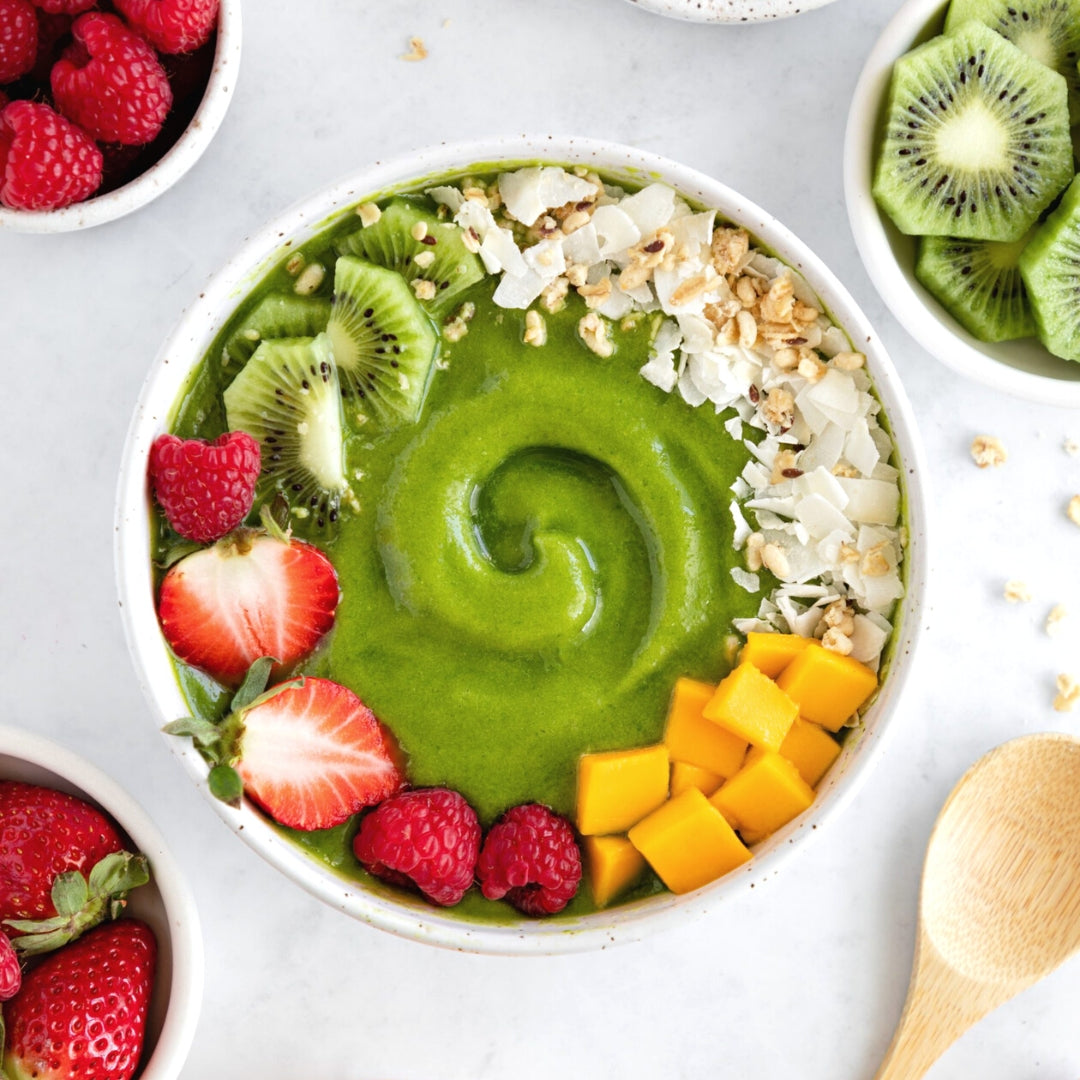 green smoothie in a bowl with wooden spoon and fresh fruits