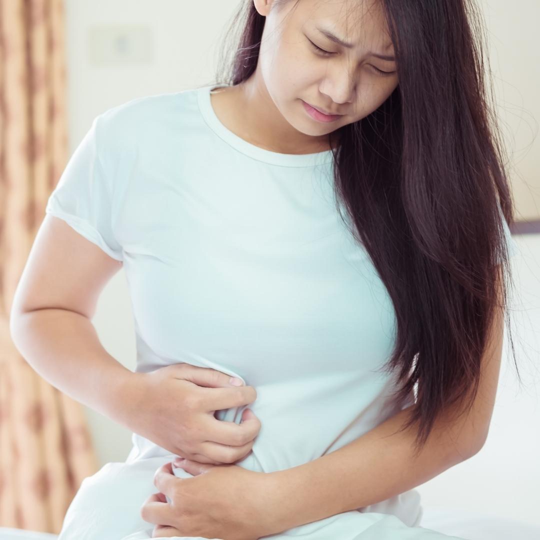 stomach ache, woman holding her stomach in pain, long hair, brown hair, white shirt