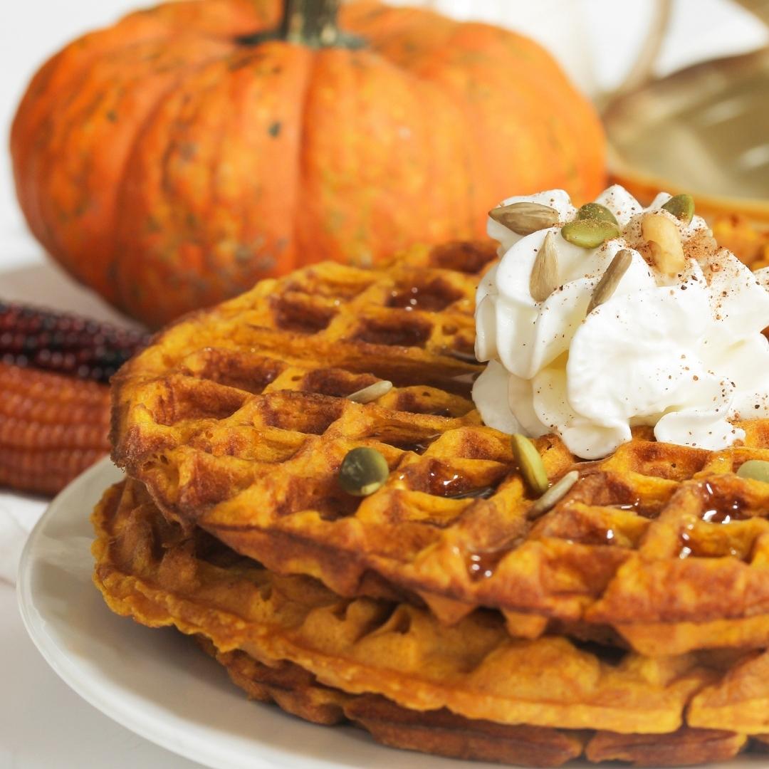 waffles with maple syrup, whip cream and pumpkin seeds on white plate, pumpkin