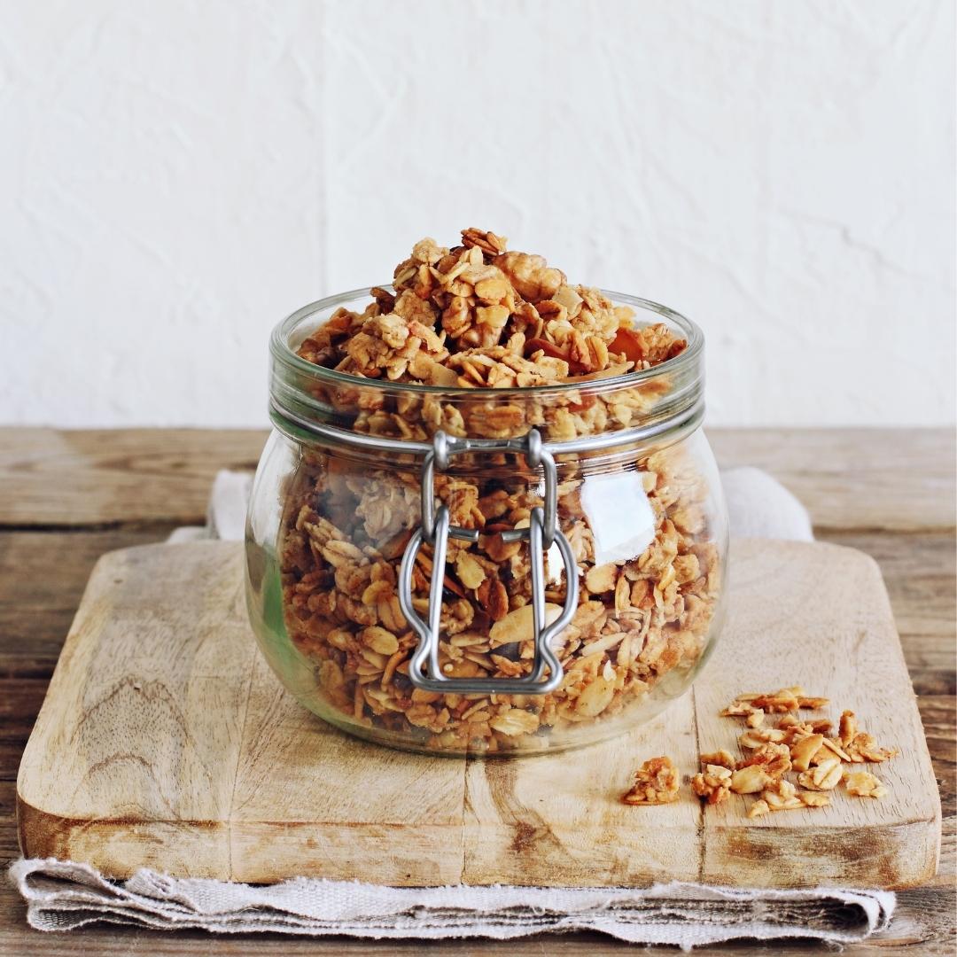 granola in small glass jar, wooden board, white towel, wooden table