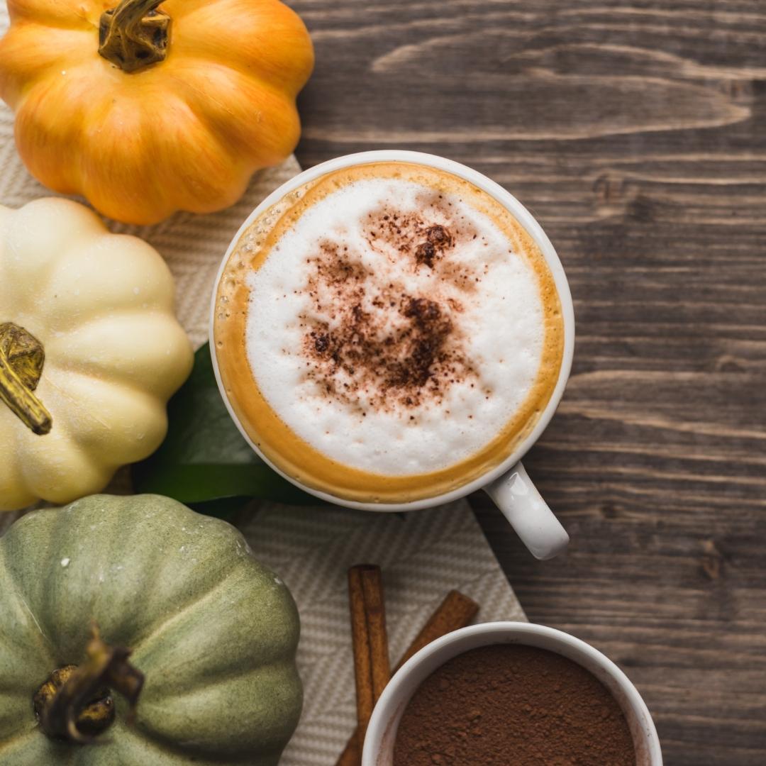 pumpkin latte with foam and sprinkled cinnamon, cinnamon sticks, brown powder, yellow pumpkin, green pumpkin, white pumpkin